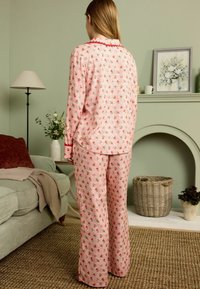 Set de pijamale roz cu modele mici de trandafiri, mâneci lungi și pantaloni largi cu o textură moale. O bordură roșie accentuează gulerul.