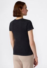 T-shirt nera a maniche corte con scollatura rotonda, caratterizzata da una texture liscia e cuciture pulite, mostrata da dietro.