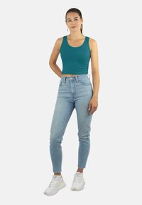 Türkises, kurz geschnittenes Tanktop mit schmalen Trägern, kombiniert mit hellblauen, hochtaillierten Skinny-Jeans und weißen Sneakers. Einfaches Design, keine Muster.