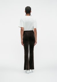 Brown corduroy flared pants with a high waist and smooth texture, paired with a plain white t-shirt and white sneakers. Back view.