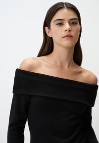 Zwarte off-the-shoulder top van geribde knitstof, met lange mouwen en een brede halslijn, gladde textuur, minimale details.