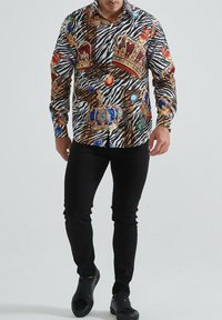 Chemise à manches longues présentant un motif zèbre audacieux, orné de couronnes dorées et de bijoux colorés. Fabriquée en tissu doux, avec une coupe structurée et un col.