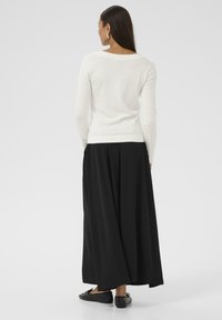 Haut blanc à manches longues avec un large col, associé à une jupe maxi noire fluide. Des ballerines noires complètent la tenue. Texture lisse, design simple.