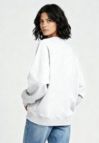 Felpa in pile grigio chiaro con collo tondo, spalle scese, polsini e orlo a coste. Modello mostrato di spalle, abbinato a un denim.