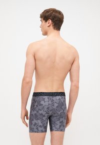 Sötét szürke férfi boxeralsó, absztrakt mintázattal. A derékpánt fekete, "ARMOUR" felirattal. Szoros illeszkedésű és rugalmas anyagból készült.