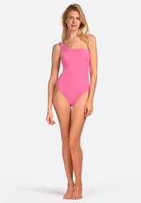 Jednoczęściowy strój kąpielowy na jedno ramię w jasnym różowym kolorze, z teksturowanym materiałem i dekoracyjnym akcentem na ramiączku. Wycięcie na biodrach dla dopasowanego wyglądu.