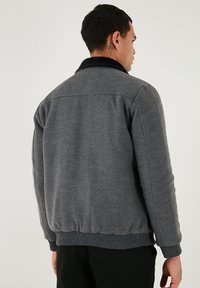 Sivá bunda vyrobená z textúrovanej tkaniny s čiernym golierom. Obsahuje rebrované manžety a pás, čo ukazuje pohodlný strih a čisté línie.