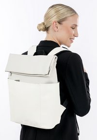 Hvid læder rygsæk med en rulle-top design, justerbare stropper, frontlomme med lynlås og minimalistisk stil; glat tekstur.