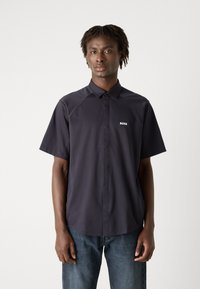 Camisa de manga curta azul-marinho com frente de botões, apresentando um colarinho espalhado e o logo branco "BOSS". Tecido suave, corte descontraído e barra arredondada.