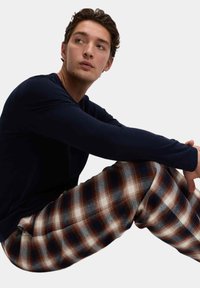 Camicia a maniche lunghe di colore blu navy abbinata a pantaloni a quadri in flanella nei toni di marrone, crema e blu navy. I pantaloni hanno una consistenza morbida e una vestibilità comoda.