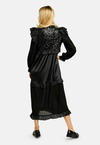 Rochie neagră cu corset strâmt din paiete și tiv cu volane în straturi. Mâneci lungi cu manșete elastice, confecționate din material texturat pentru un plus de detaliu.