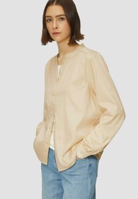 Lichtbeige knoopshirt met een ronde halslijn, lange mouwen en een relaxed fit, gecombineerd met blauwe jeans. Beschikt over een gladde stoftextuur.