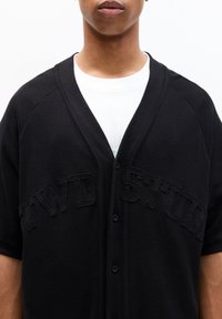 Schwarze Strickjacke mit V-Ausschnitt, kurzen Ärmeln und geprägtem "FWD STUD"-Text auf der Vorderseite sowie Knopfverschluss.