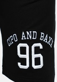 Shorts en tissu noir avec broderie blanche "CIPO AND BAXX" au-dessus du numéro "96". Le design est simple avec une texture douce.