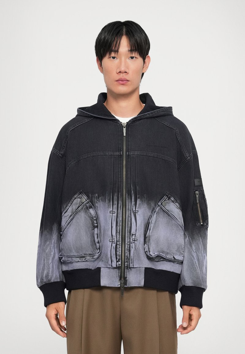 Hooded denim jacket featuring a gradient black to gray color, large front pockets, and ribbed cuffs. Zipper front detail and contrasting textures.