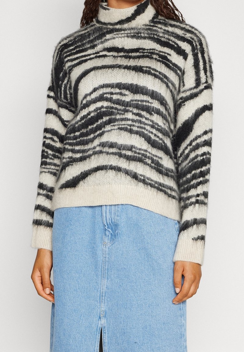 Pull en mélange de laine avec un col montant, base crème avec des rayures abstraites noires et grises, coupe ample et poignets côtelés.