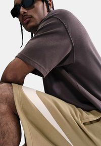 Camisa marrón de manga corta con tejido texturizado y corte relajado; pantalones cortos beige con un gran logo blanco de Nike y bolsillos laterales.