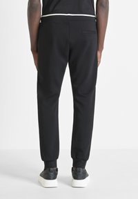 Pantalones de chándal negros con puños ajustados, hechos de tela suave. Presentan un bolsillo trasero y un detalle de cinturilla blanca en contraste. Combinados con zapatillas negras.