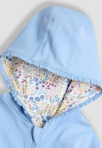 Sudadera de bebé azul claro con borde acampanado y forro interior con un patrón de flores coloridas y caballos blancos.