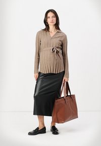 Top en tricot côtelé marron, jupe midi en cuir plissé noire, et sac fourre-tout marron ; le mannequin se tient debout avec des mocassins noirs, sur un fond simple.
