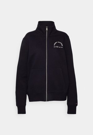 Sudadera negra con cremallera, cuello alto, bolsillos delanteros y texto blanco "Tommy Hilfiger New York Est. 1985" en el pecho.