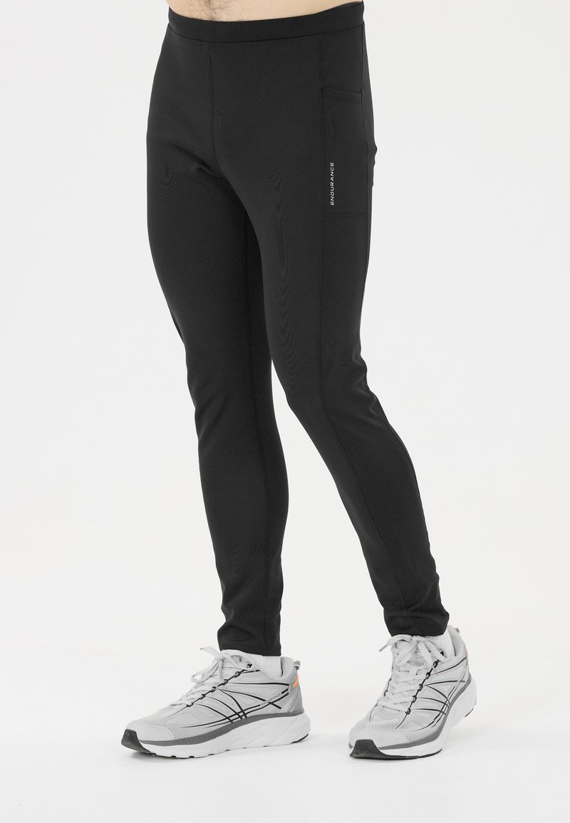 Zwarte sportbroek gemaakt van rekbaar materiaal met een slanke pasvorm. Voorzien van zijzakken en een platte tailleband, gecombineerd met grijze hardloopschoenen.