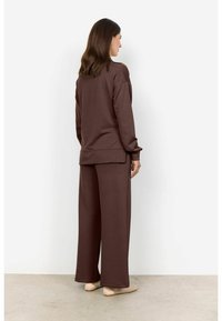 Completo con pullover marrone e pantaloni a gamba larga, realizzato in un materiale morbido, con una vestibilità rilassata e un orlo posteriore leggermente più lungo.