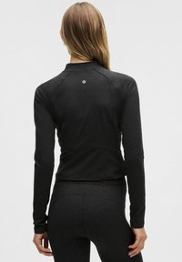 Schwarzes langärmliges Sportoberteil aus weichem, dehnbarem Stoff. Verfügt über einen hohen Kragen und dezentes Logodetail auf der Rückseite. Eng anliegendes Design.