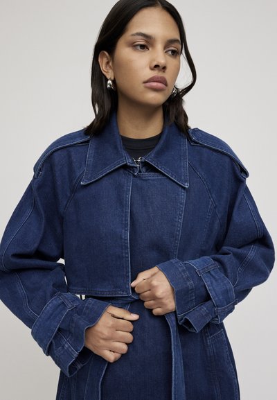 Giacca di jeans blu scuro con un design strutturato, ampio colletto e maniche larghe, con cintura in vita e dettagli di cucitura visibili.