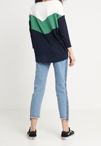 Granatowy i zielony oversize'owy top z białymi ramionami; rękawy do łokcia. W komplecie z jasnoniebieskimi jeansami z postrzępionymi nogawkami i czarnymi butami płóciennymi.