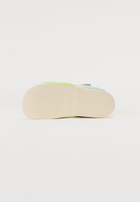 Podošva obuvi Adidas s textúrovaným gumovým povrchom, s akcentmi v zelenej a modrej farbe a imprintom loga, prevažne v off-white farbe.