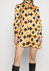 Robe chemise en soie présentant un motif géométrique orange, noir et blanc, avec un devant boutonné et de longues manches à poignets froncés.