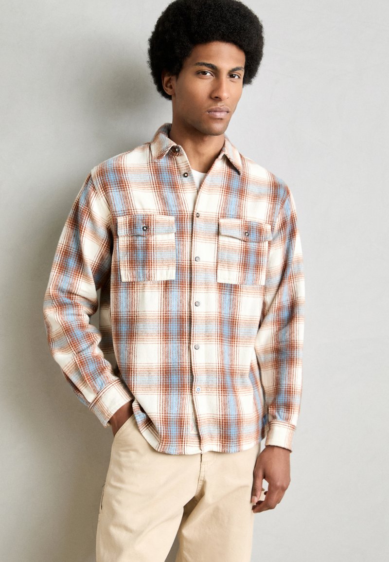 Plaid flannel shirt in cream, blue, and rust colors; features button-down design, two front pockets, and long sleeves.