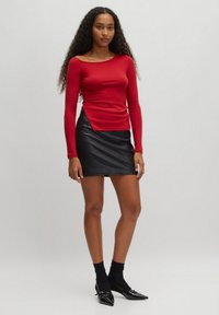 Rood geribd langslid top met een off-shoulder ontwerp, gecombineerd met een aansluitende zwarte nepleer minirok. Zwarte sokken en puntige ballerina's maken de look compleet.