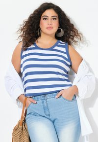 Canottiera a righe blu e bianche con scollo rotondo, abbinata a jeans azzurri e una camicia bianca con bottoni, completata da una borsa intrecciata marrone.