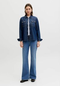 Tumeda sinist värvi teksajope kahe rinnatasku, valgete nööpide ja pikkade varrukatega. Koos hele siniste kellukakujuliste teksade ja mustade kingadega.