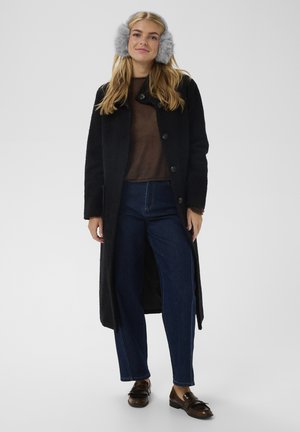 Čierny kabát zo zmesi vlny s veľkými gombíkmi, hnedý sveter a tmavomodré rifle s vysokým pásom. Oblečenie dopĺňajú sivé náušníky z umelého kožušiny.