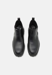 Bottes de cheville en cuir noir avec panneaux élastiques sur les côtés et tirants. Design à orteils ronds avec semelle en caoutchouc texturé. Fini lisse, détails minimaux.