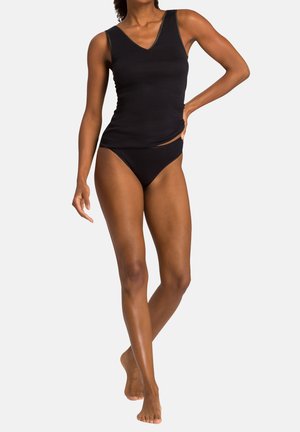 Kobieta ubrana w czarny bezrękawnik i pasujące czarne bikini, stojąca boso na jednolitym tle.