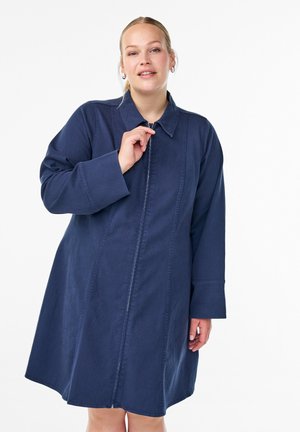 Denim obleka v mornarsko modri barvi, ki ima ovratnik, dolge rokave, sprednji zadrgo in navpične šive. Gladka tekstura in dolžina do kolen.