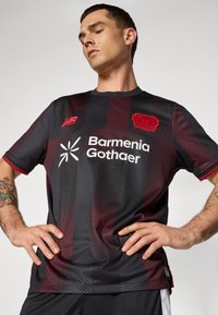 Sort og rød stribet sportsjersey med en glat tekstur, der har et logo og branding i hvid. Korte ærmer og rund hals design.