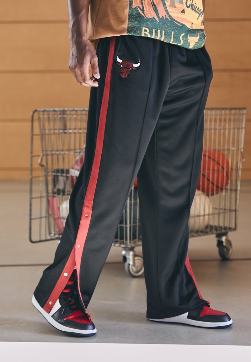 Crne sportske hlače s crvenim bočnim prugama, s vezom loga bika. Uparene s crnim i crvenim tenisicama koje imaju slip-on dizajn.