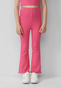 Roze geribde leggings met een flared zoom, gecombineerd met een bijpassende cropped top en witte sneakers. De stof heeft een gladde textuur.