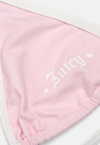 Ροζ ανοιχτό μπουστάκι μπικίνι με άσπρη επένδυση και άσπρο γκοθ στυλ κείμενο "Juicy" πλαισιωμένο από δύο μικρά εικονίδια καρδιάς.