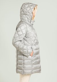 Gesteppter silberner Steppmantel mit Kapuze, mit glatter Textur, diagonalen Nähten und Seitentaschen, der bis zur Mitte der Oberschenkel reicht.