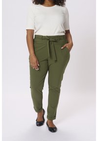 Pantaloni verde oliva con cintura a cravatta, caratterizzati da una vestibilità affusolata e orli arrotolati, abbinati a un top corto crema e ballerine nere.