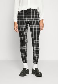Calças xadrez preto e branco com um design ajustado, apresentando um fecho de correr e tecido elástico, combinadas com meias brancas e mocassins pretos chunky.