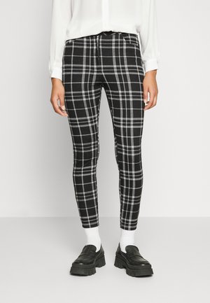 Calças xadrez preto e branco com um design ajustado, apresentando um fecho de correr e tecido elástico, combinadas com meias brancas e mocassins pretos chunky.
