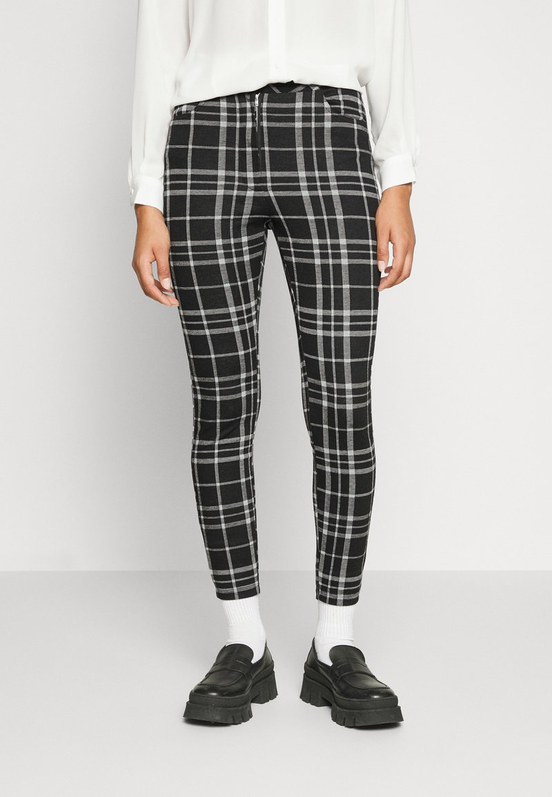 Calças xadrez preto e branco com um design ajustado, apresentando um fecho de correr e tecido elástico, combinadas com meias brancas e mocassins pretos chunky.