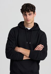 Felpa nera con cappuccio, tasca a marsupio, cappuccio con coulisse e polsini in costina, caratterizzata da una superficie liscia e un design comodo.